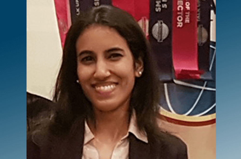 Woman in black suit jacket posing in front of banner